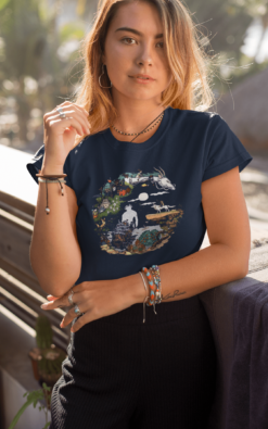 A blonde woman wearing a navy-blue t-shirt featuring a crescent moon-inspired Studio Ghibli design, posing near palm trees.