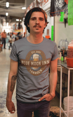 Man wearing Blue Moon Inn Varrock vintage t-shirt standing casually indoors at a market.