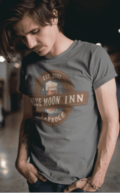 Man wearing Blue Moon Inn Varrock unisex t-shirt in daylight, showcasing casual street style.