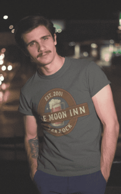 Lifestyle shot of man modeling Blue Moon Inn Varrock unisex t-shirt in casual outdoor setting.