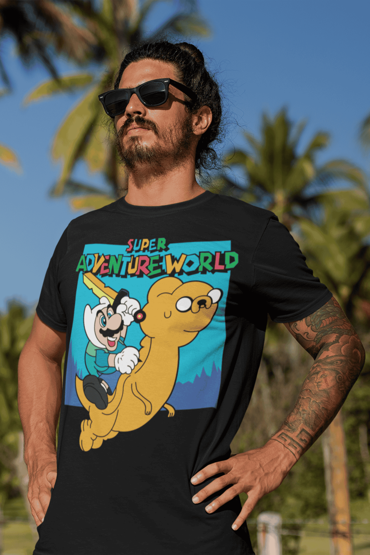 Male model wearing Super Adventureworld black tee featuring Mario riding Jake from Adventure Time, sunglasses on, standing at the beach.