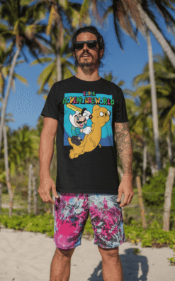 Smiling male model wearing Super Adventureworld black tee with Mario and Jake, sunglasses on, standing on a sunny beach.