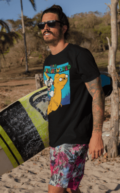 Tattooed male surfer wearing Super Adventureworld black tee featuring Mario and Jake at the beach, smiling confidently.