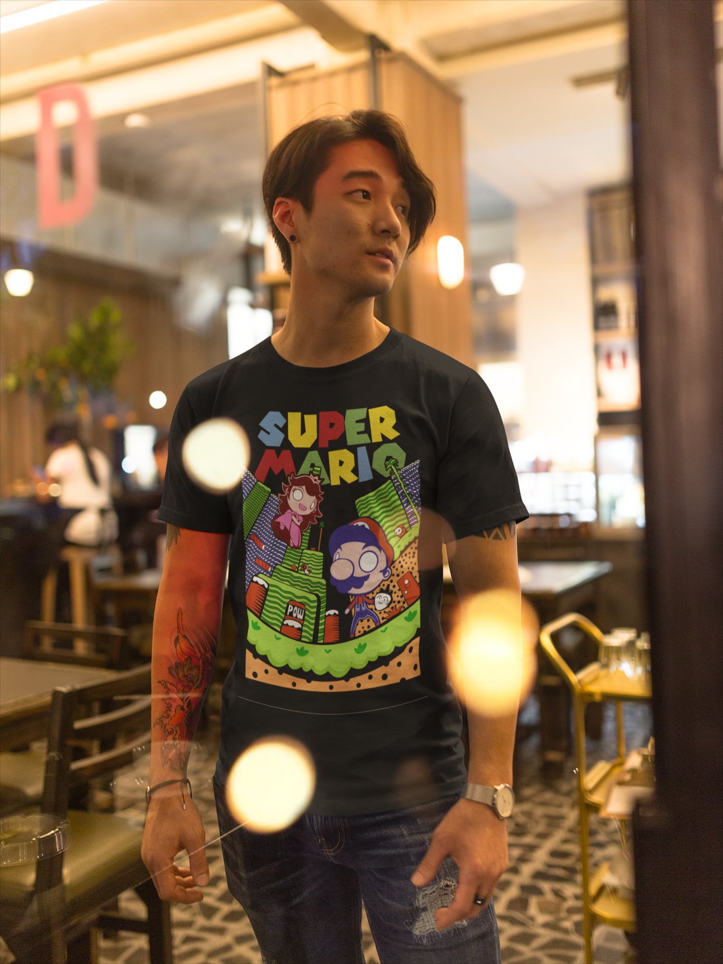 Asian man wearing black Super Mario unisex t-shirt standing in a restaurant with warm lighting