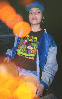Woman sitting wearing black Super Mario t-shirt with colorful lights and denim jacket