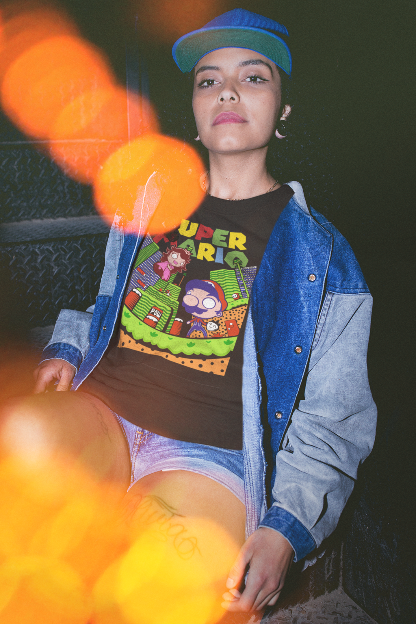 Woman sitting wearing black Super Mario t-shirt with colorful lights and denim jacket