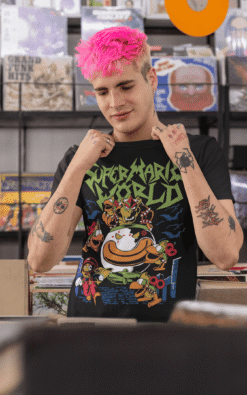Man with pink hair wearing a heavy metal Super Mario World tee browsing records in a store.